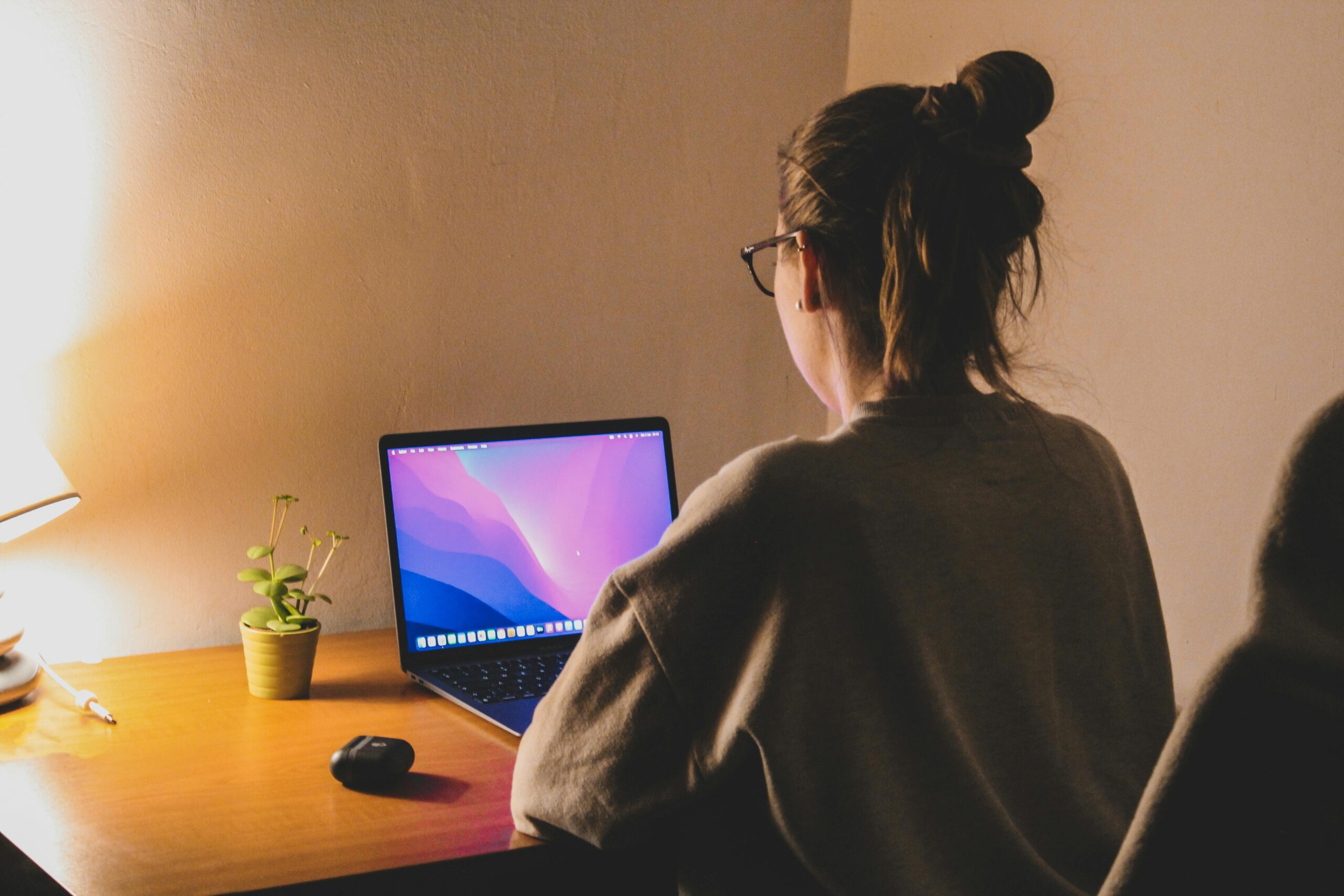 Eine Frau sitzt abends vor einem Laptop, neben ihr spendeteine Tischleuchte Licht.